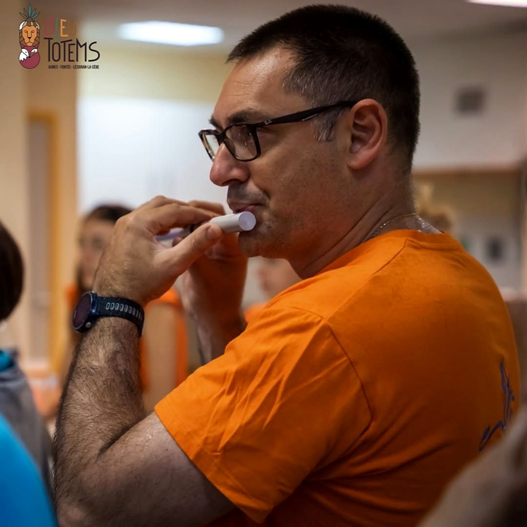 Participant en t-shirt orange jouant d'un instrument lors d'un atelier à Aumes.