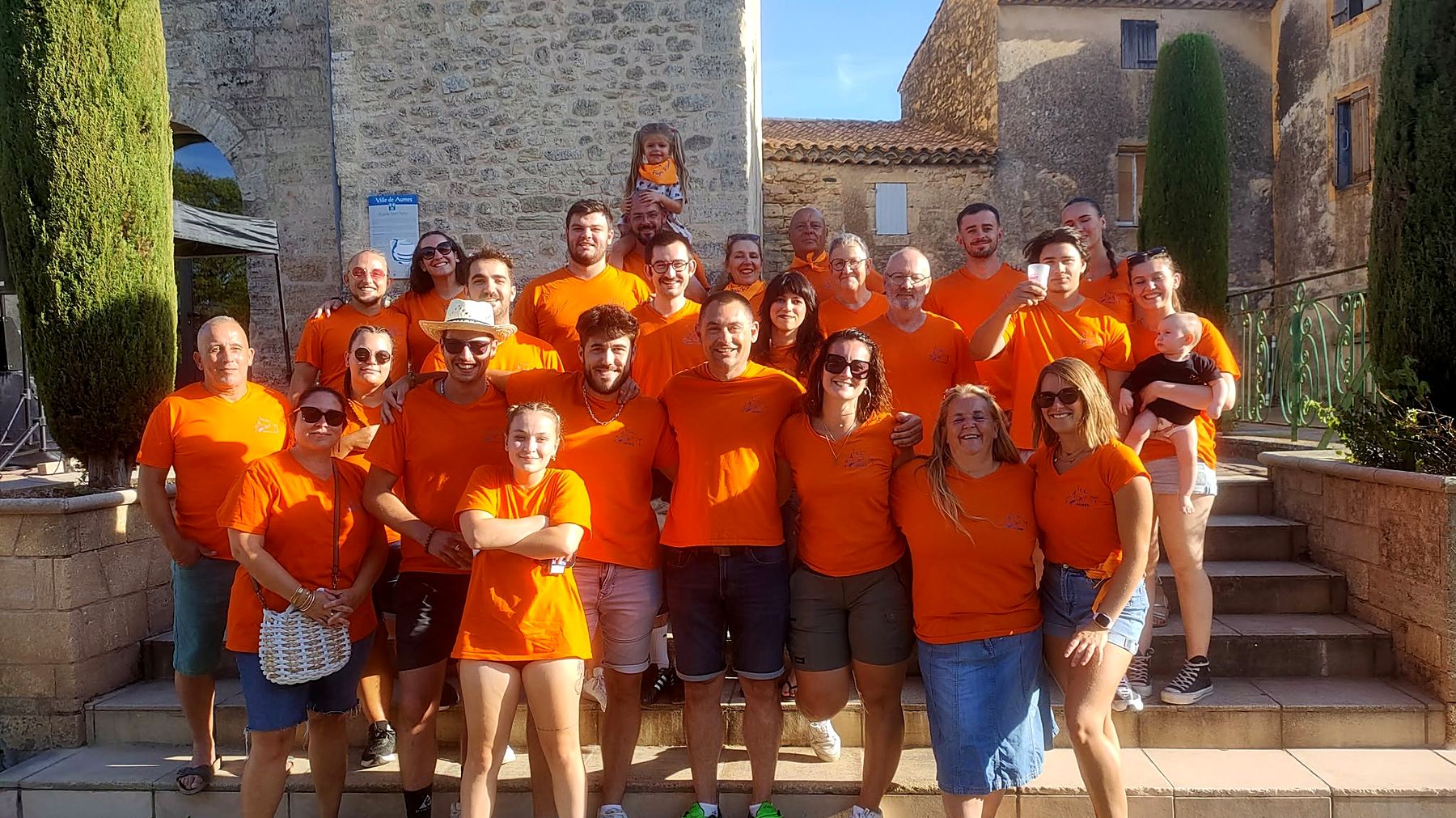 Une trentaine de bénévoles du Foyer Rural de Aumes en t-shirts orange, de tous âges, réunis devant la chapelle Saint-Pierre.