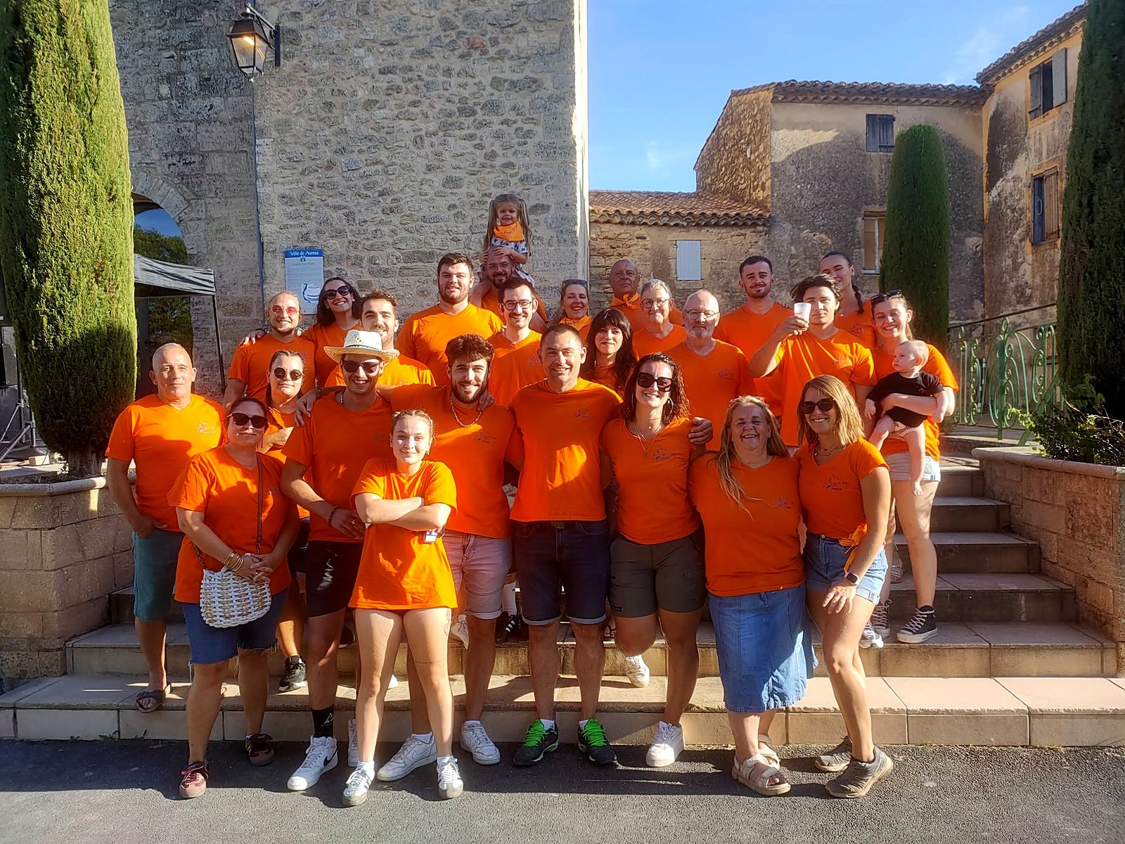Une trentaine de bénévoles du Foyer Rural de Aumes en t-shirts orange, de tous âges, devant la chapelle Saint-Pierre.