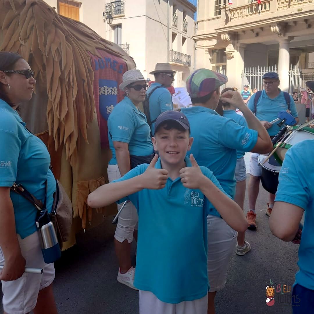 Défilé du totem dans les rues de Aumes, participants en polos bleus et tambours.