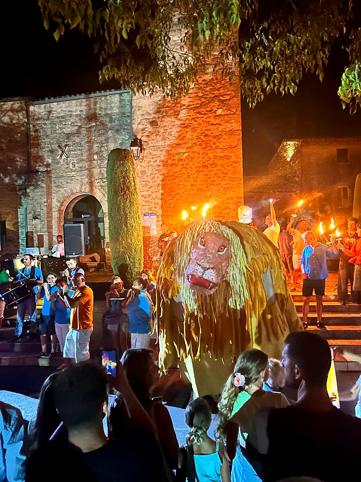 Léo, le lion totémique de Aumes, porté sur la place du village à la nuit tombée, entouré de musiciens et de porteurs de flambeaux.