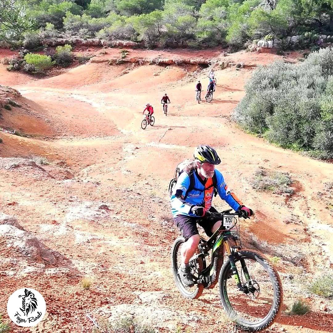 Vététistes descendant une large piste ocre au milieu de la garrigue.