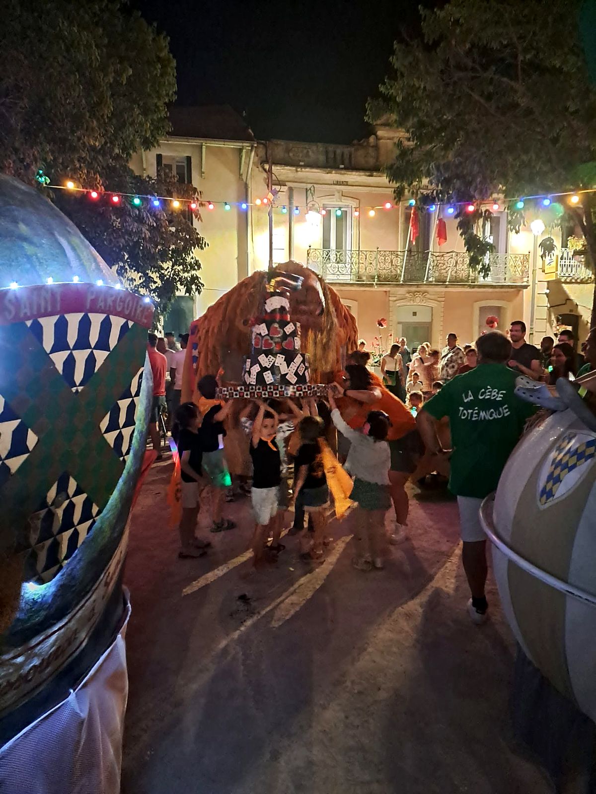 Défilé nocturne des animaux totémiques sur la place de Aumes, sous les guirlandes.